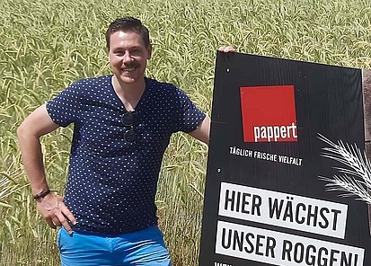 Partner-Landwirt Christian Bug auf einem Roggenfeld stehend - neben ihm ein Roggenschild platziert.