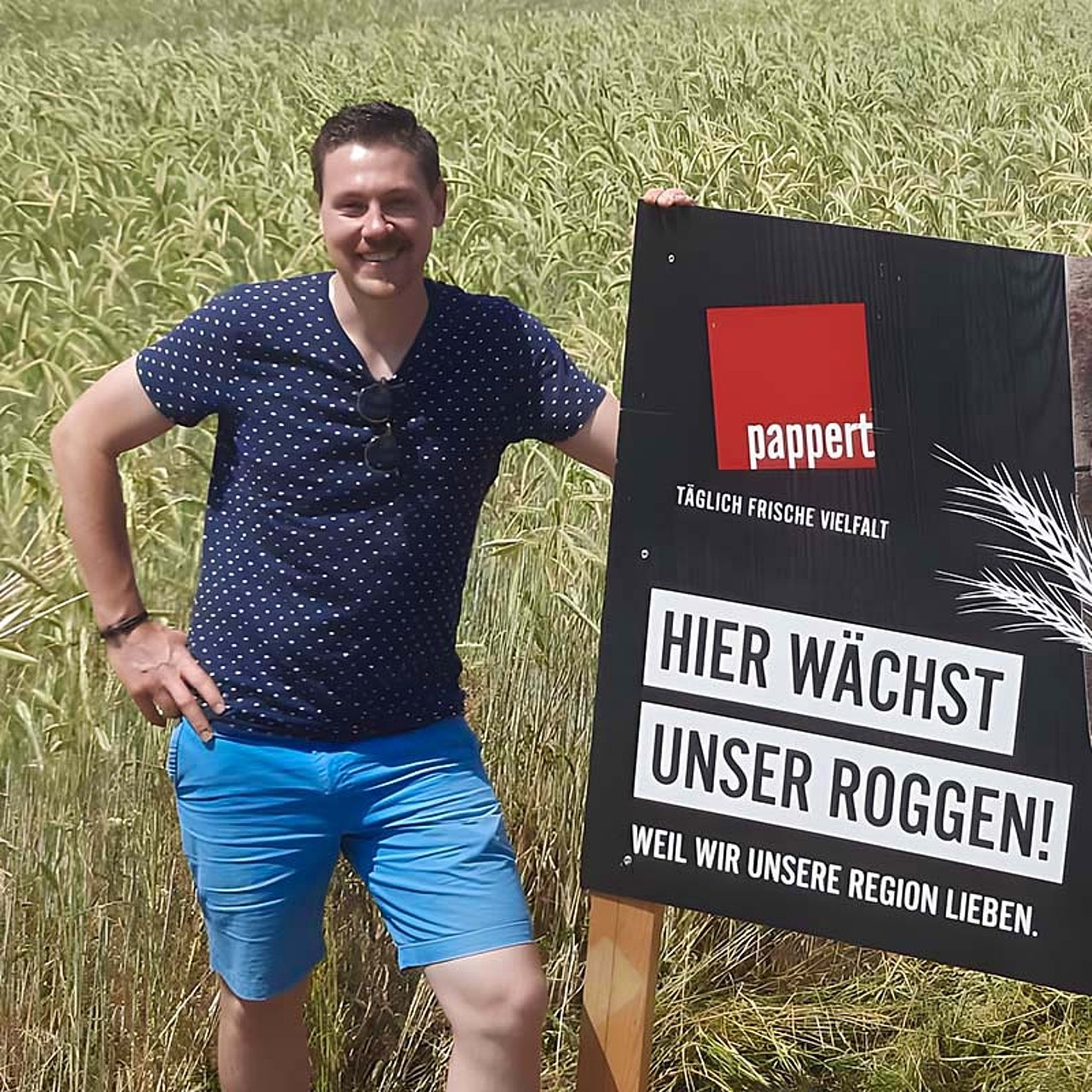 Partner-Landwirt Christian Bug auf einem Roggenfeld stehend - neben ihm ein Roggenschild platziert.