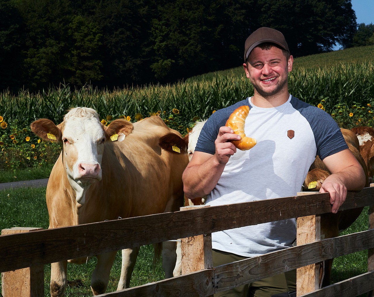 Landwirt Max Helfrich steht freudig vor seiner Weide mit Kühen und hält ein Milchhörnchen von Pappert in der Hand.