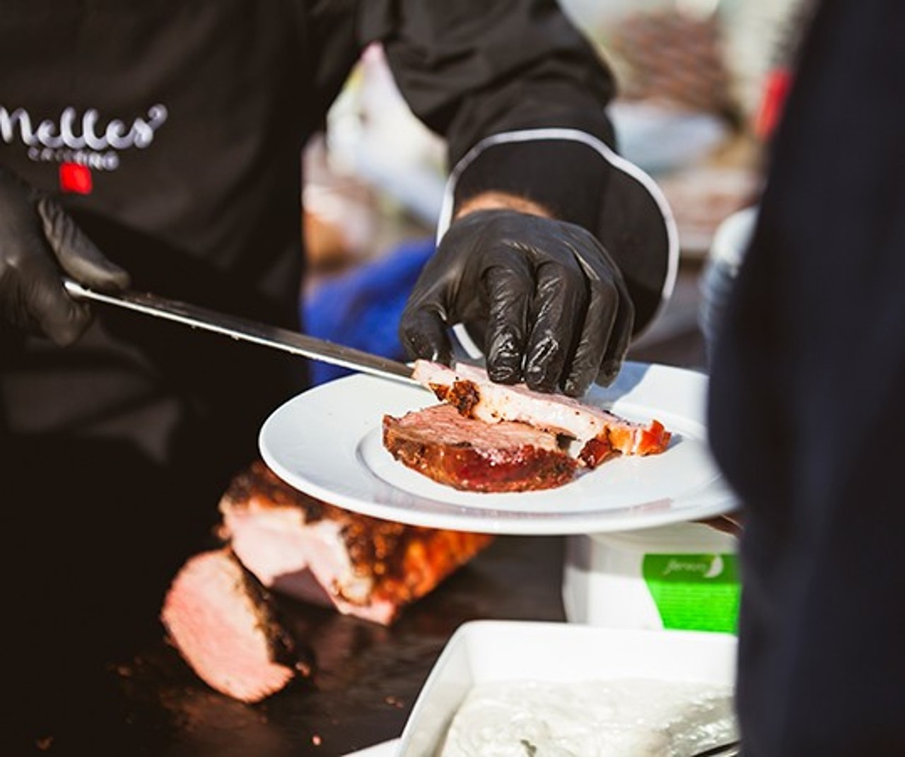 Ein Koch von Caterer Sven Nelles schneidet beim Mittagstisch gebratenes Fleisch und serviert es auf einen Teller.