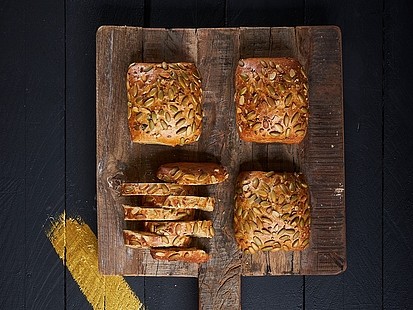 Das KürbisFit der Bäckerei Pappert wird mit steirischem Kürbiskernöl und frischen Karotten gebacken Mehrere KürbisFit der Bäckerei Pappert auf einem rustikalen Holzbrett, auf dunklem Holzhintergrund platziert.