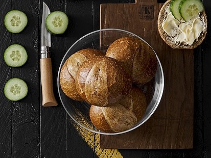 Das Roggenbrötchen der Bäckerei Pappert aus regionalem Roggen aus Hessen und Bayern Mehrere Roggenbrötchen der Bäckerei Pappert in einer Glasschale auf dunklem Holzhintergrund, daneben ein halbiertes Roggenbrötchen, mit Butter und Gurkenscheiben belegt.