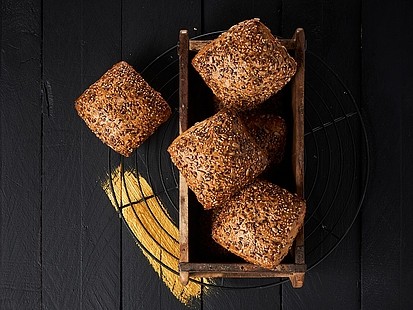 Das Dreisaatbrötchen der Bäckerei Pappert erhält durch geröstete Saaten seinen kernig-nussigen Geschmack Mehrere Dreisaatbrötchen der Bäckerei Pappert in einer rustikalen Holzschale, auf dunklem Holzhintergrund platziert.