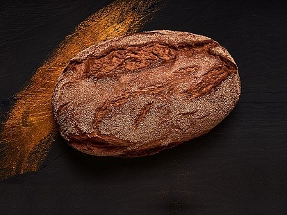 Die Rhöner Kruste der Bäckerei Pappert bekommt ihren ursprünglichen Geschmack auch dank der besonderen Körnung Die Rhöner Kruste der Bäckerei Pappert auf einem schwarzem Holzhintergrund platziert.
