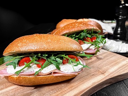 Das Tomaten-Mozzarella-Schinken Krusti auf einer Holzplatte vor dunklem Hintergrund platziert. 