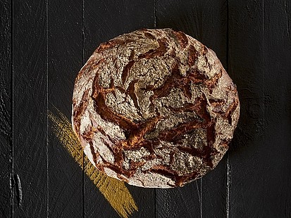 Das Rusti XL der Bäckerei Pappert ist ein rustikales auf Stein gebackenes Roggenmischbrot Das Rusti XL der Bäckerei Pappert auf einem schwarzem Holzhintergrund platziert.