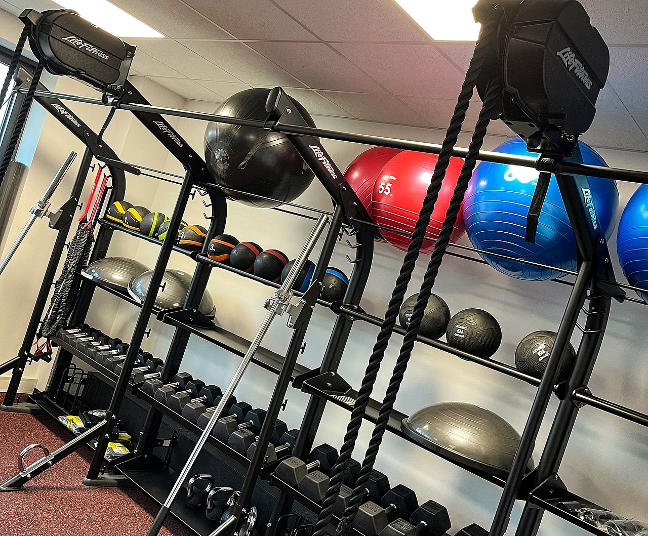 Ausstattung des Mitarbeiter-Fitnessraums zeigt Hanteln, Kettlebells, Medizinbälle, Fitnessbänder, Balance-Boards, große Gymnastikbällen und Trainingsgeräte.