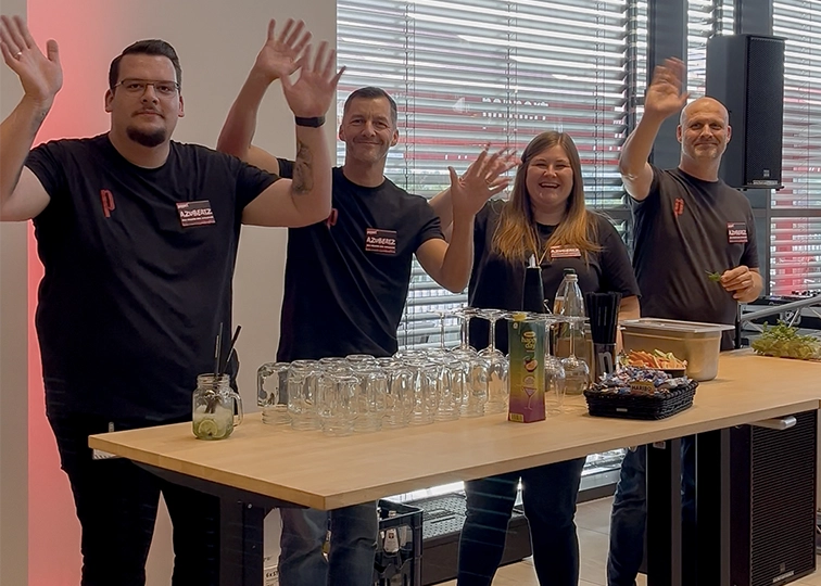 Eine Gruppe von Menschen steht am Tisch und winkt freundlich