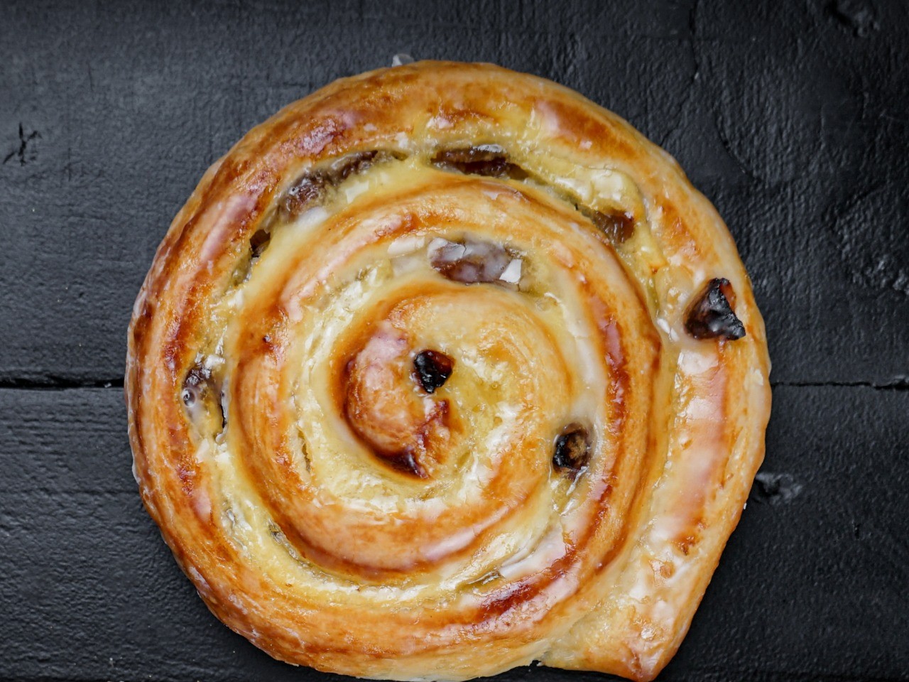 Die-Rosinenschnecke-der-Bäckerei-Pappert-ist-gefüllt-mit-Rosinen-und-zartem-Pudding-auf-schwarzem-Holzhintergrund