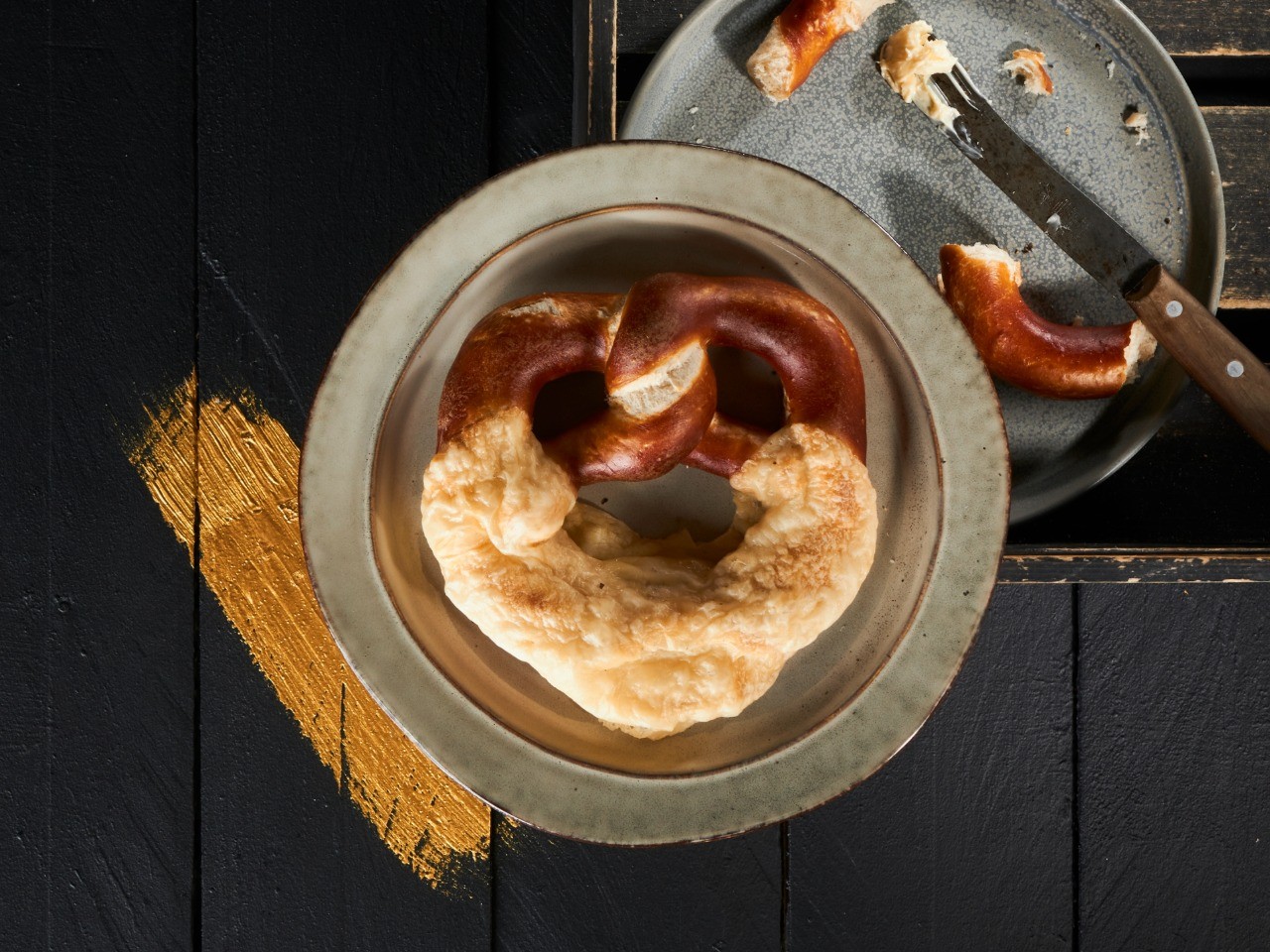 Die-Käsebrezel-der-Bäckerei-Pappert-ist-ein-klassisches-Laugengebäck-mit-Käse-verfeinert-auf-dunklem-Holzhintergrund