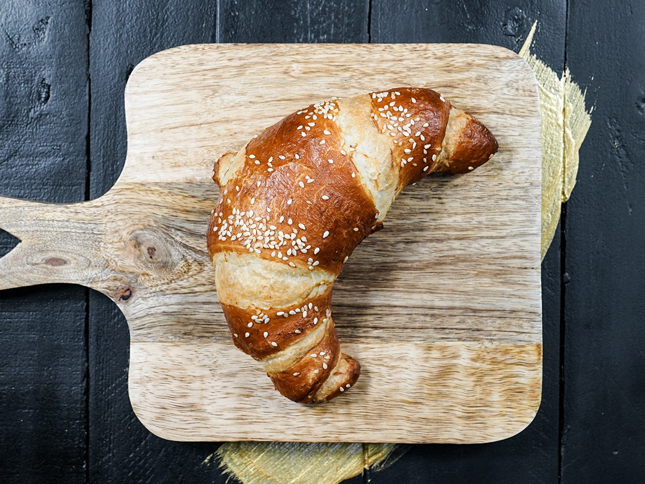 Das Kräuterfrisch-Croissant der Bäckerei Pappert liegend auf einem Holzbrettchen und platziert auf einem dunklen Holzhintergrund.